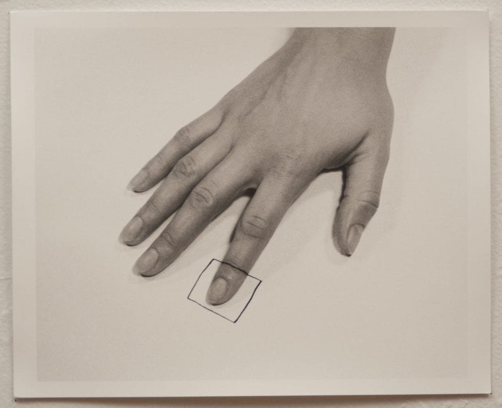 A photo of a black and white photograph with a hand, palm facing down, on paper. A square is drawn on the tip of the index finger and on the paper.