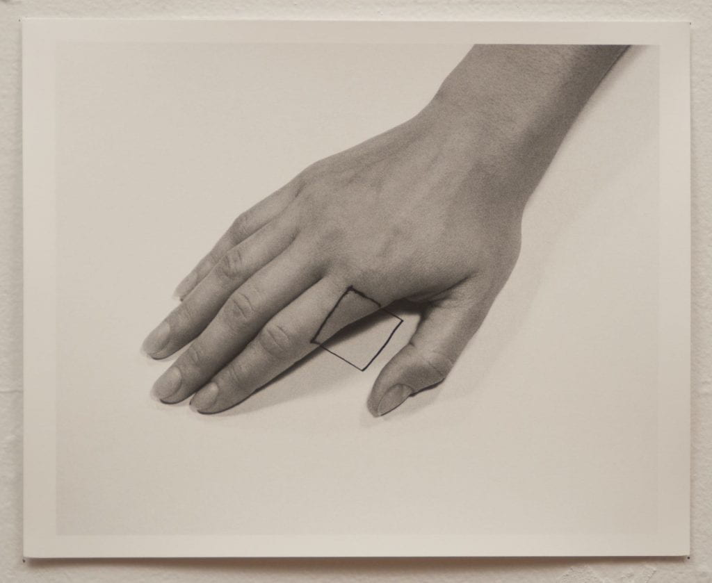 A photo of a black and white photograph with a hand, palm facing down, on paper. A square is drawn on
the tip of the index finger and on the paper.