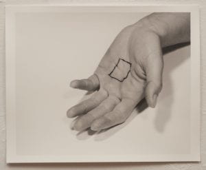 A photo of a black and white photograph with a hand, palm facing up, on paper. A square is drawn on the palm of the hand.