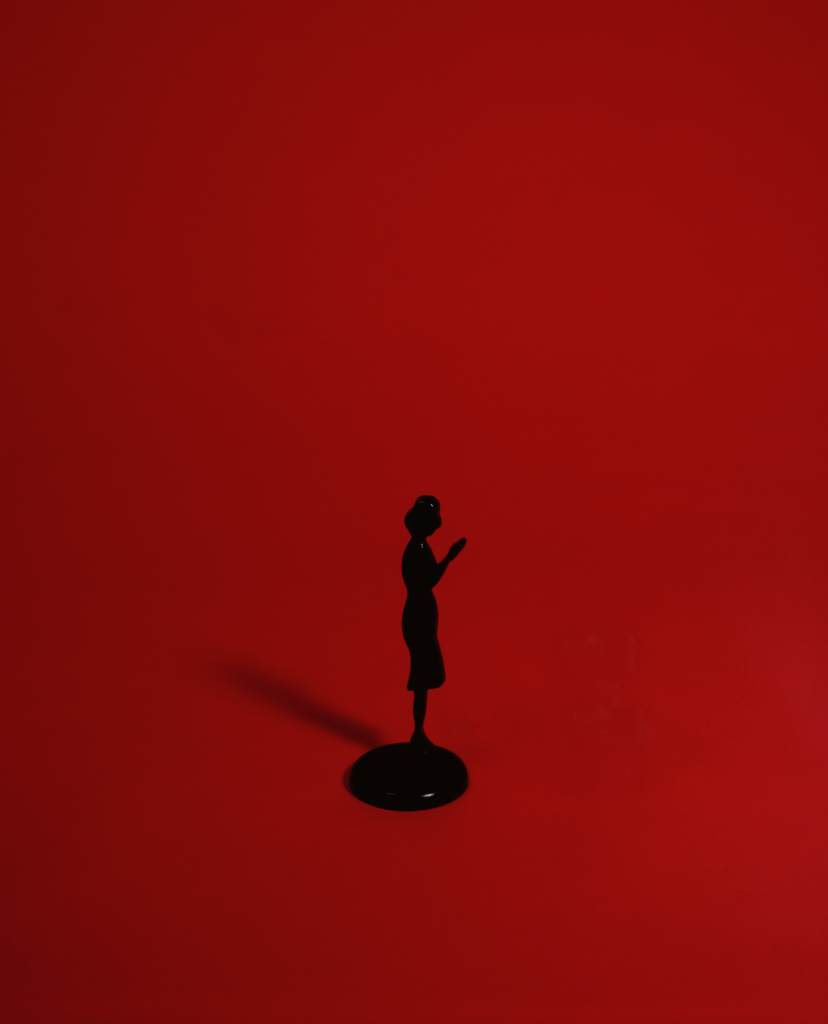 A video still of a black figurine wearing a dress in front of a bright, solid red background. 