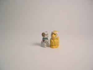A print of a spotted dog figure staring at a yellow monkey salt shaker, which glances to the side. The dog has a blue collar and the monkey has white hair.