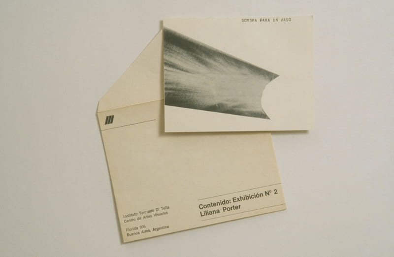 A photograph of an off-white envelope and postcard. A water glass’s shadow is printed on the latter, with the text “Sombra Para Un Vaso.”