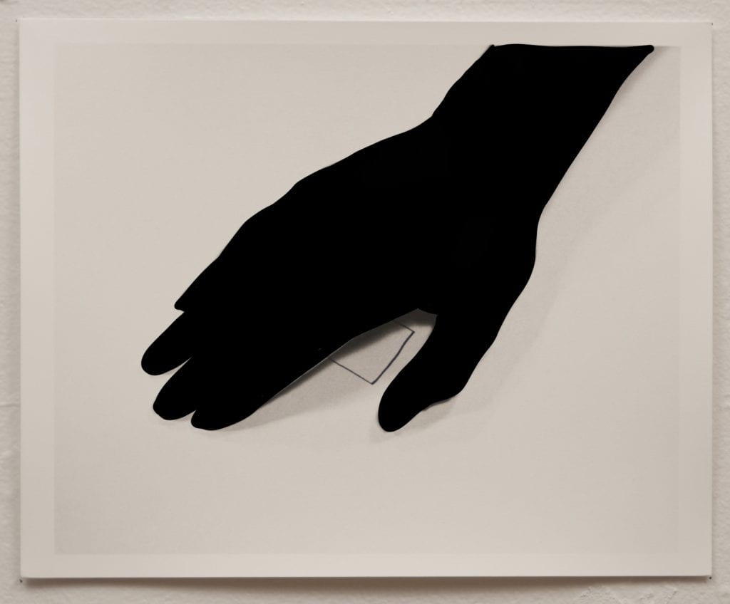 A black outline of a hand, palm facing down, on paper. A part of a square is drawn on the paper.