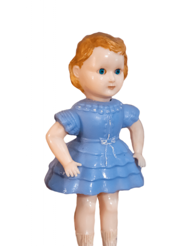 A photo of a doll with orange hair, blue eyes, and a blue dress. She stands with her arms raised slightly against a white background.