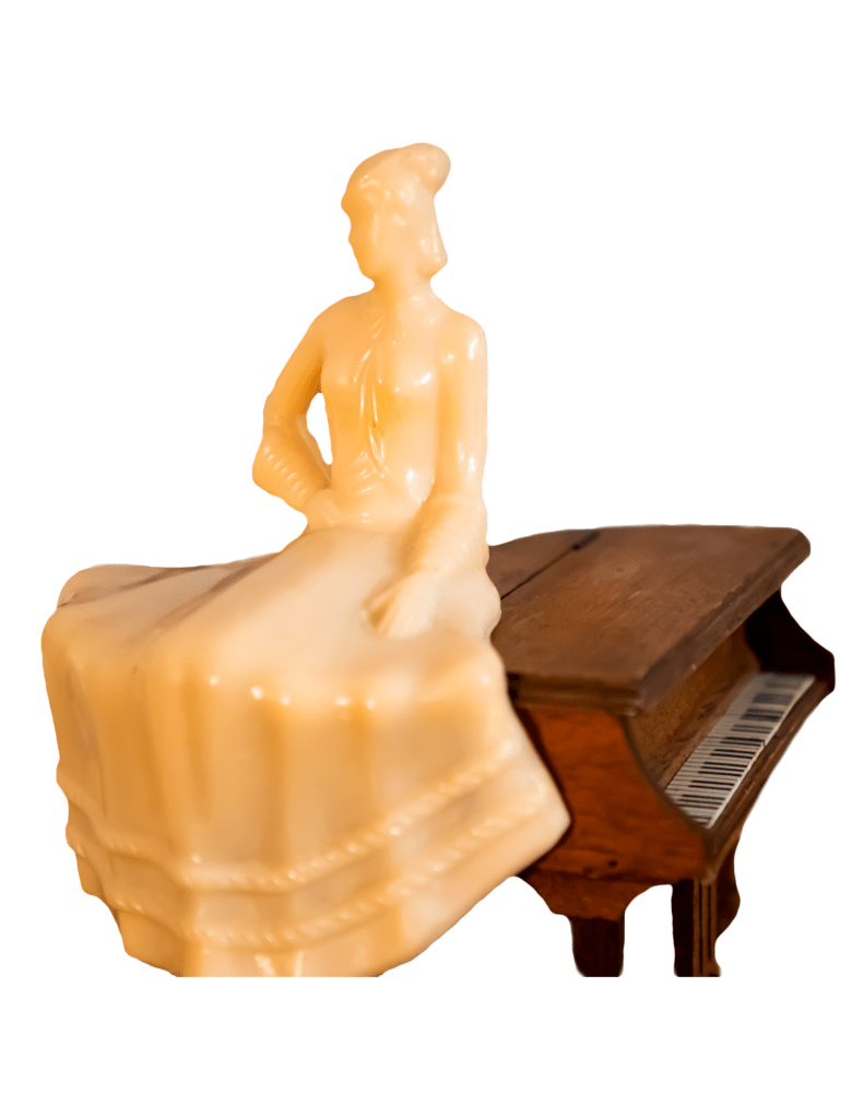 A photo of a cream-colored ceramic woman in a dress. She sits atop a wooden piano against a white background.